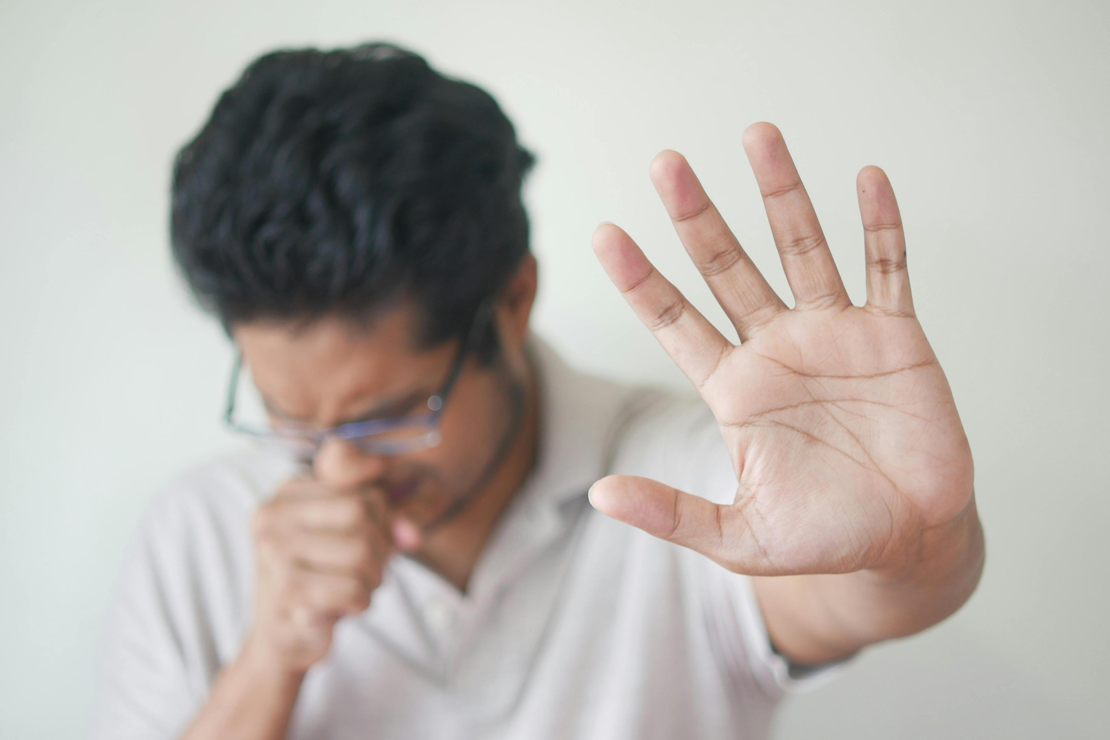 man coughing and holding one hand up to create space