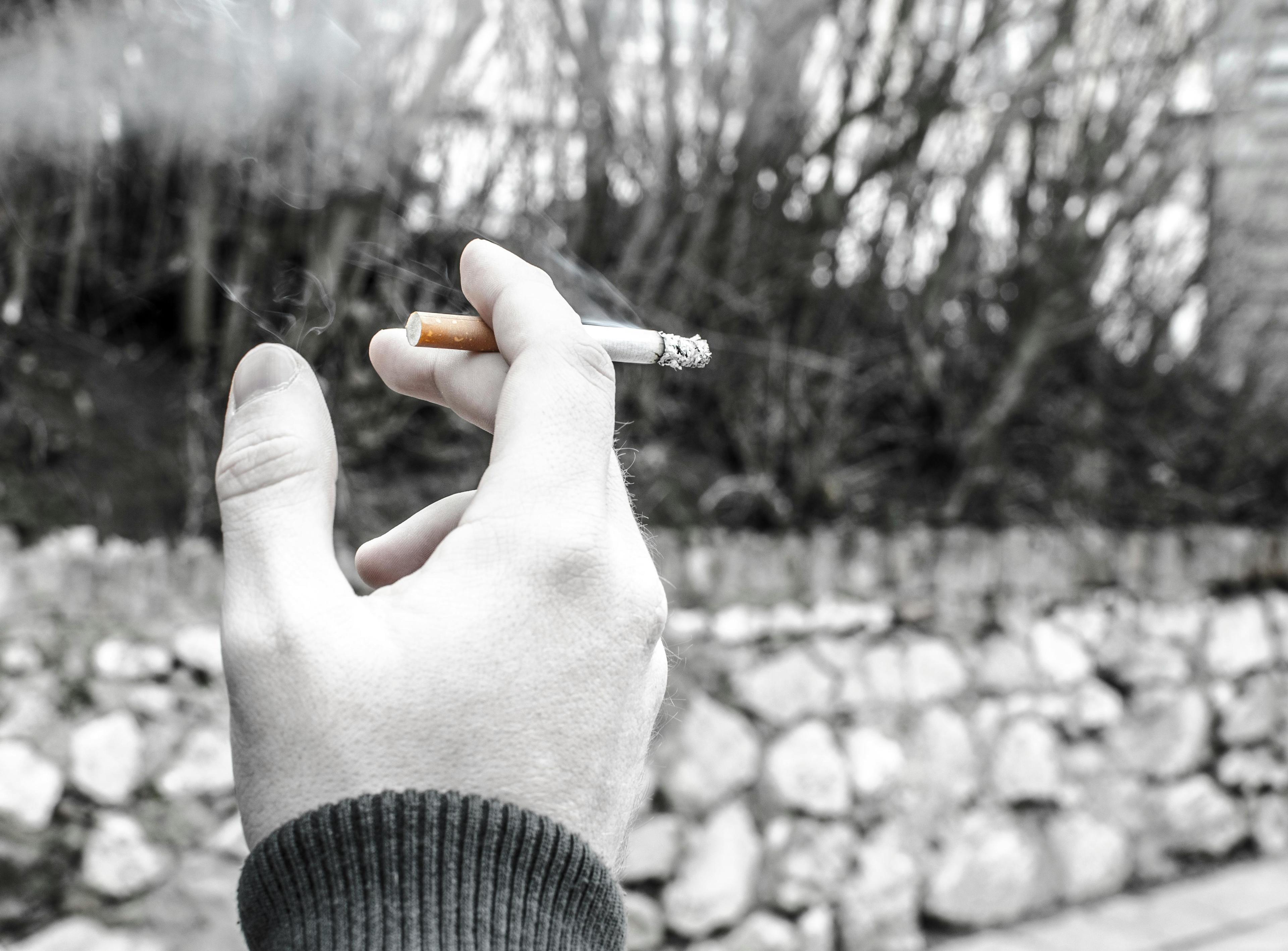 Black and white photo of male hand holding a burning cigarette