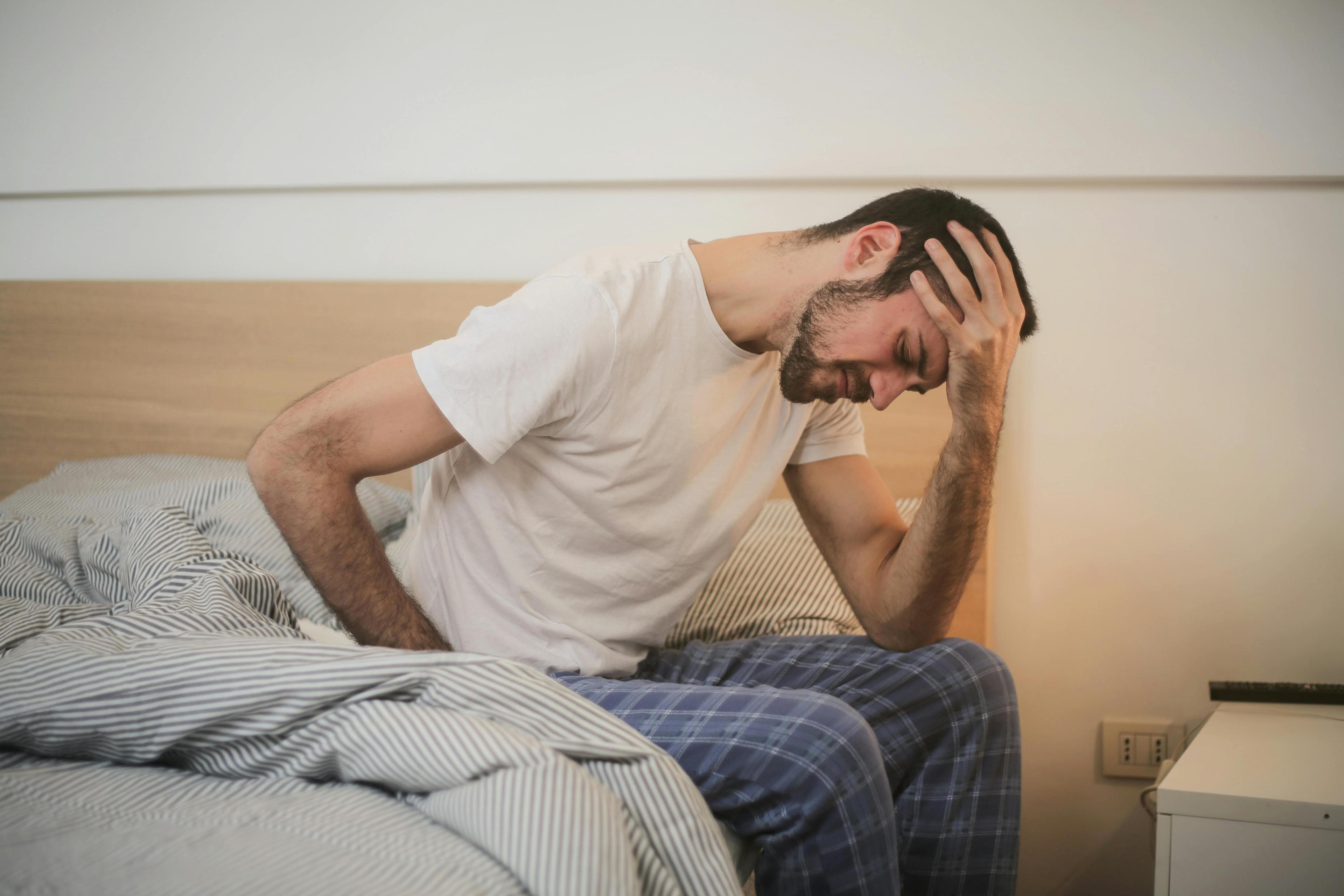 man waking up in bed feeling ill and holding his head